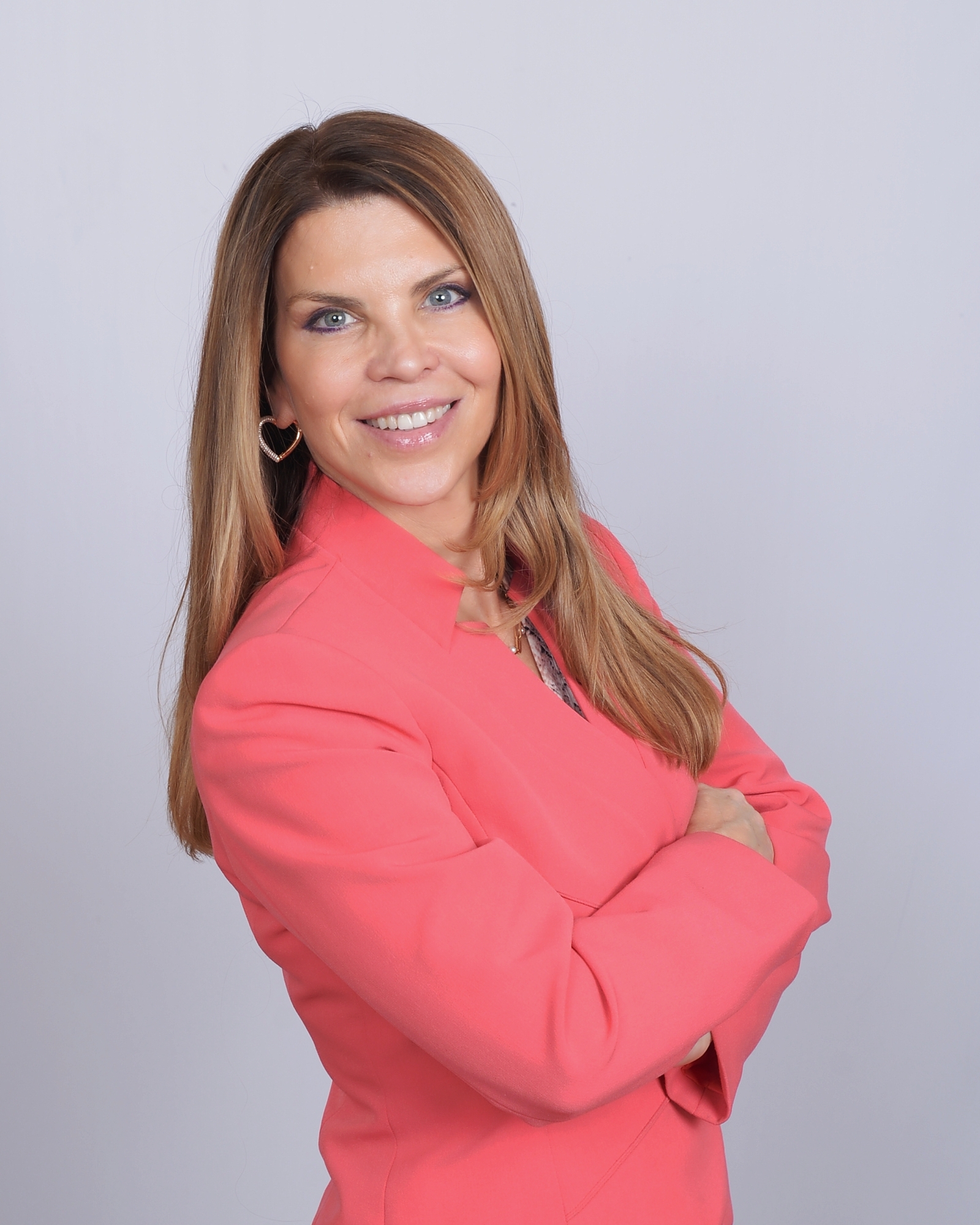 Professional headshot of a smiling woman wearing a coral blazer against a light gray background