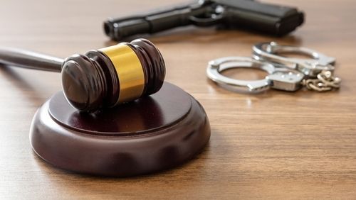 Búa thẩm phán và súng ngắn trên bàn làm việc của luật sư. Khái niệm về tội phạm, hình phạt giết người. Bàn gỗ trong tòa án, cận cảnh.