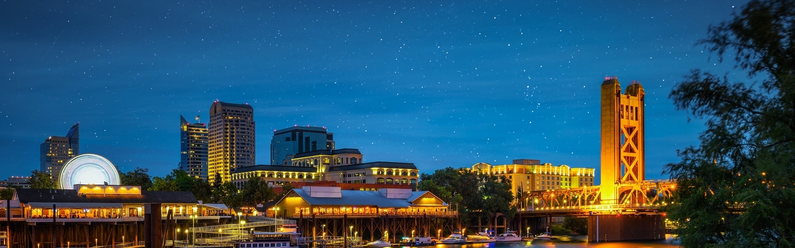 Gold Tower Bridge and Sacramento River in Sacramento, California, photographed from River Walk Park at night with stars in the sky.